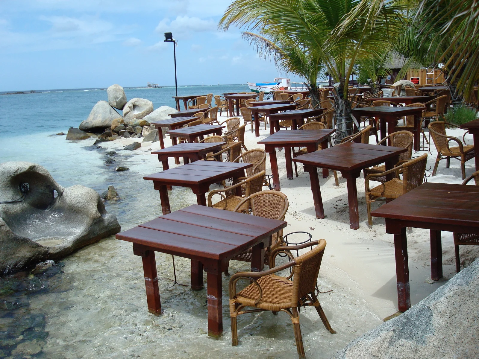 Wooden tables and Rattan chairs lined up in the shore for a lovely beachside dining on one of the best restaurants in Aruba