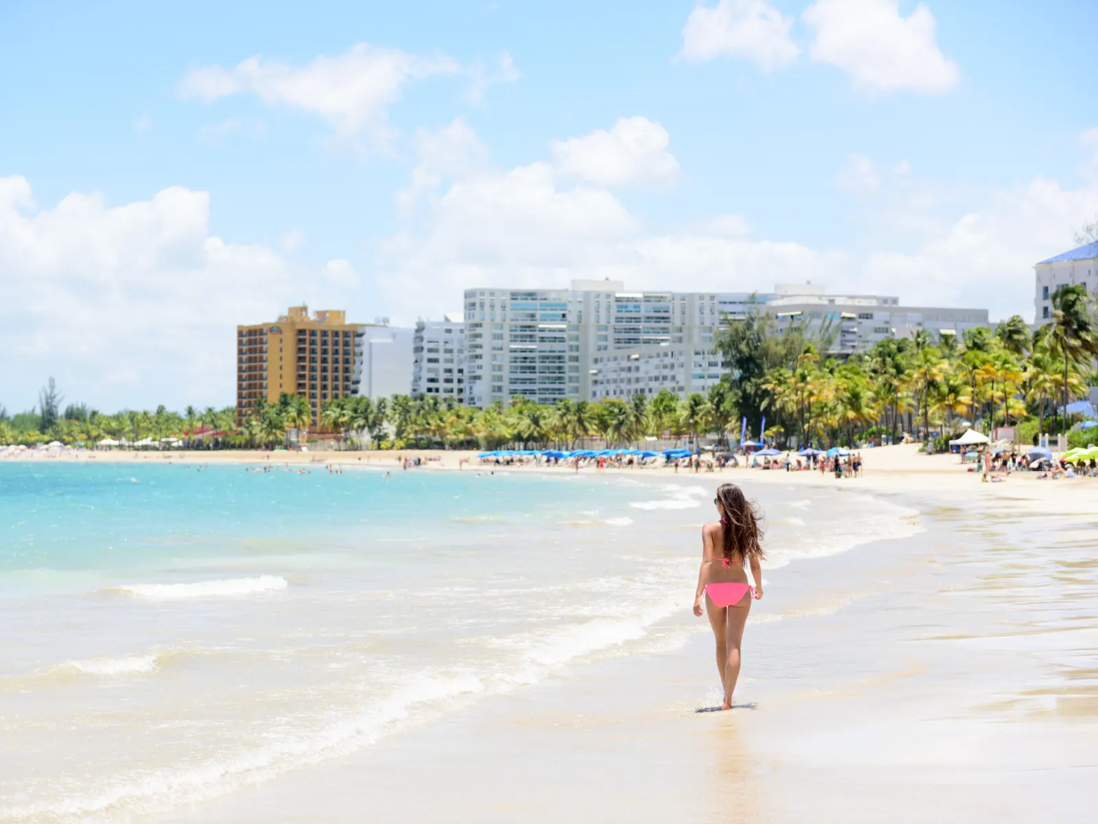 Woman walking on Isla Verde, one of the best beaches in Puerto Rico, in a pink bikini