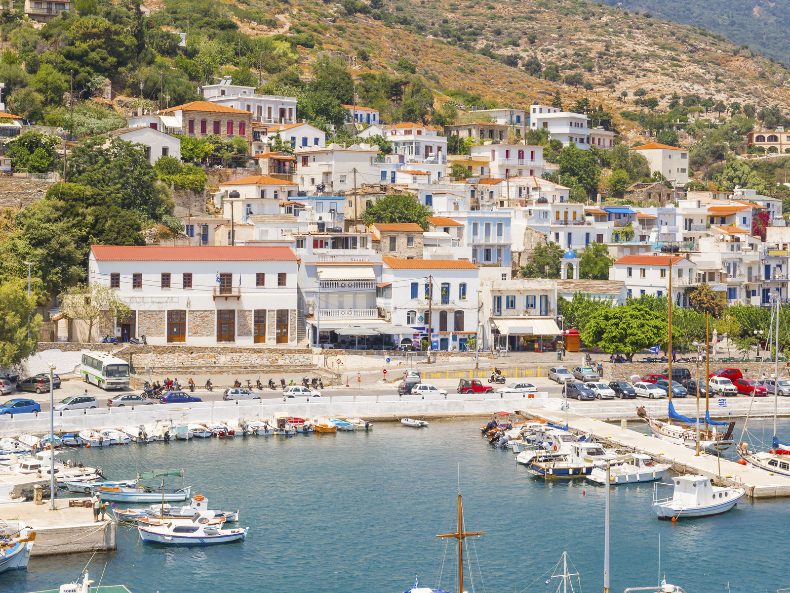 Cars parked on a coastal road and boats docked on a port in Agios Kirikos City at Ikaria island, one of the best islands in Greece to visit