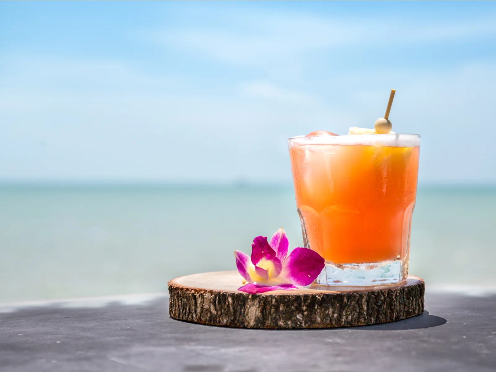 A refreshing glass of Mai Tai on a circular wooden piece with a flower served cold during a hot summer at On The Rocks, one of the best restaurants in Kona, Hawaii