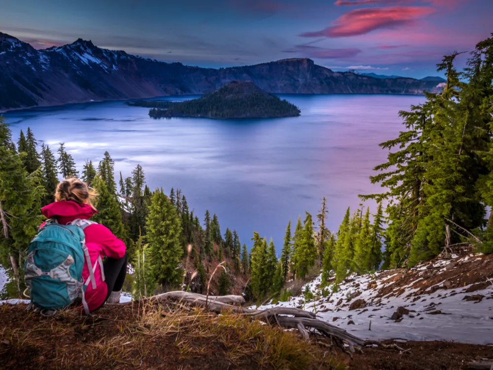 A backpacker girl viewing the still Crater Lake in Oregon, a piece on the best lakes in the U.S., at dusk