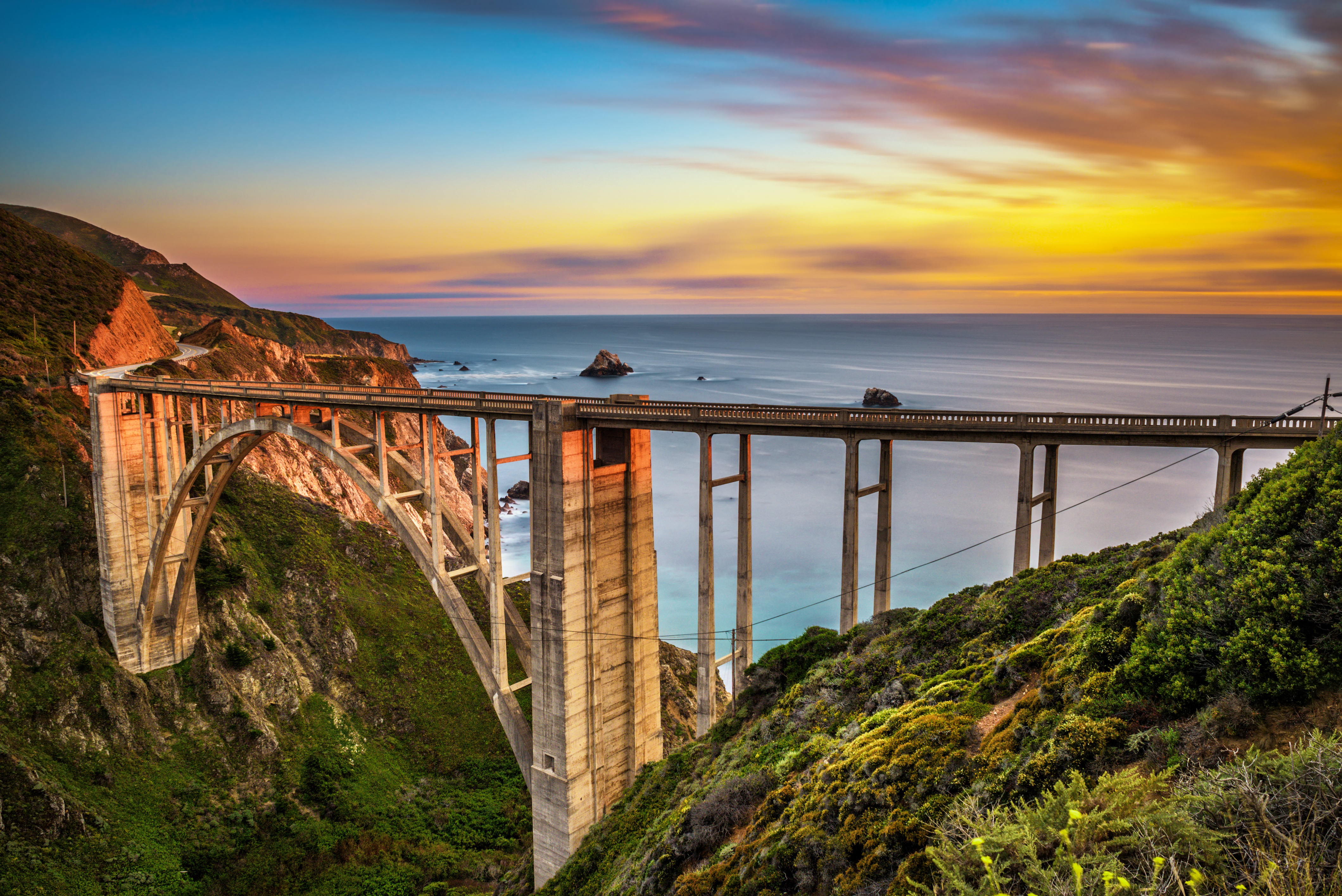 Bixby bridge pictured during the best time to visit California with the sun setting over the ocean and rocks