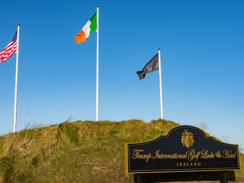 Three flags raised from tall poles and a golden sign of Trump International Golf Links and Hotel, one of the best golf courses in Ireland
