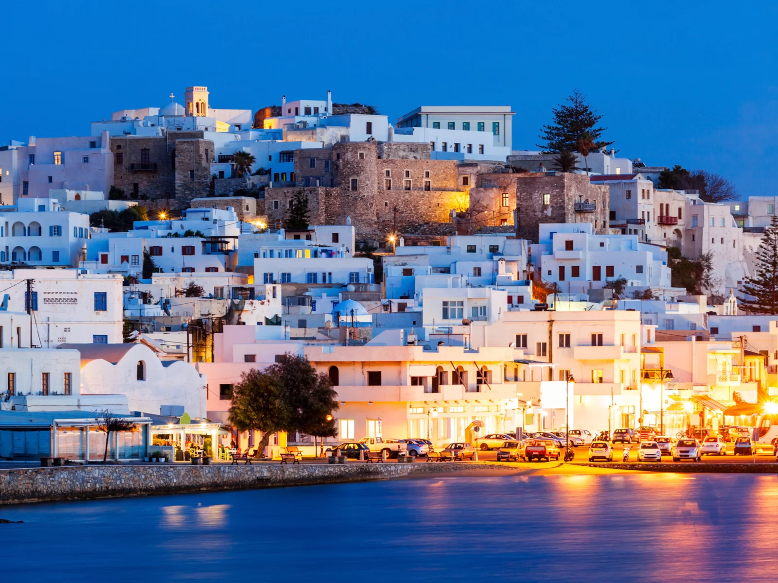 Peaceful dusk at Naxos Island, one of the best islands in Greece to visit, street lamps reflected on the still sea waters, and quiet white houses