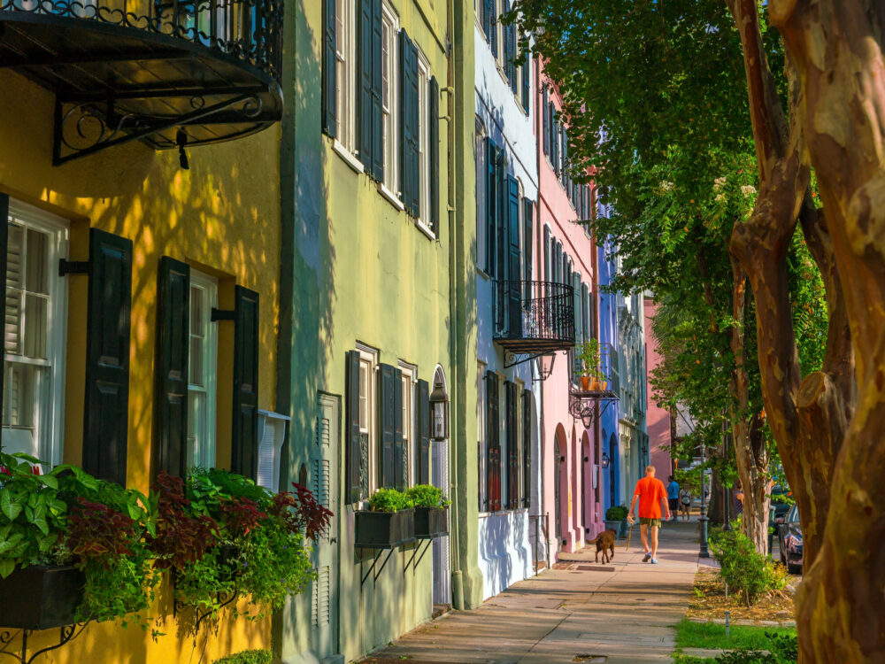 Guy walking from one of the best hotels in Charleston SC by rainbow row, a bunch of neat and colorful homes