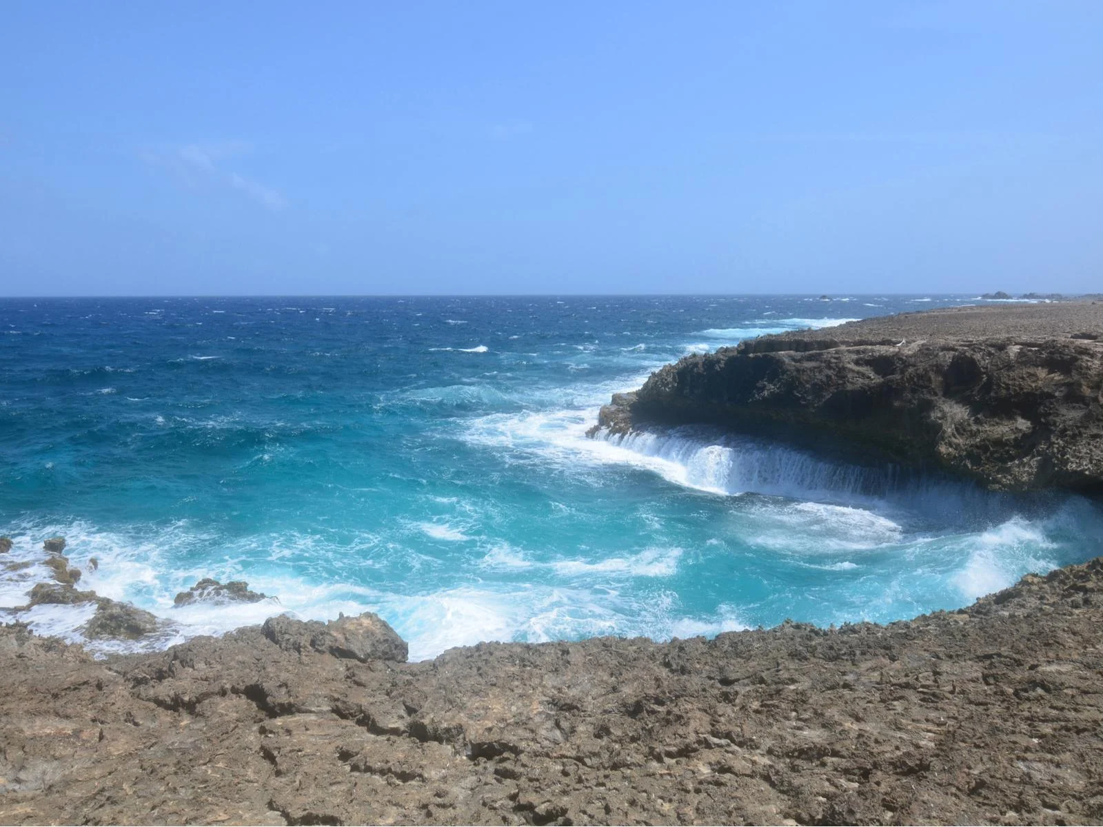 A cliff-like rocky coast of Daimari Beach, one of the best beaches in Aruba, with its deep and creamy waters due to strong waves crashing