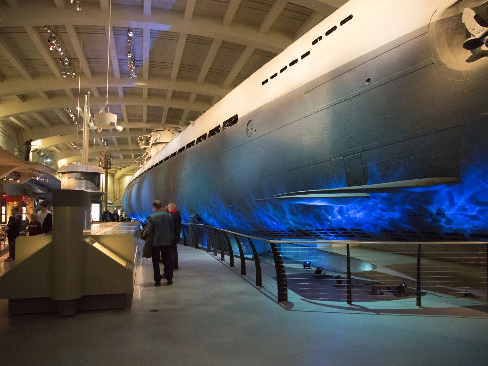 Several adult and kids viewing exhibits at the Main Hall at Museum of Science and Industry in Chicago, one of the best science museums in America, with a large ship lit with blue lamp to imitate the waves 