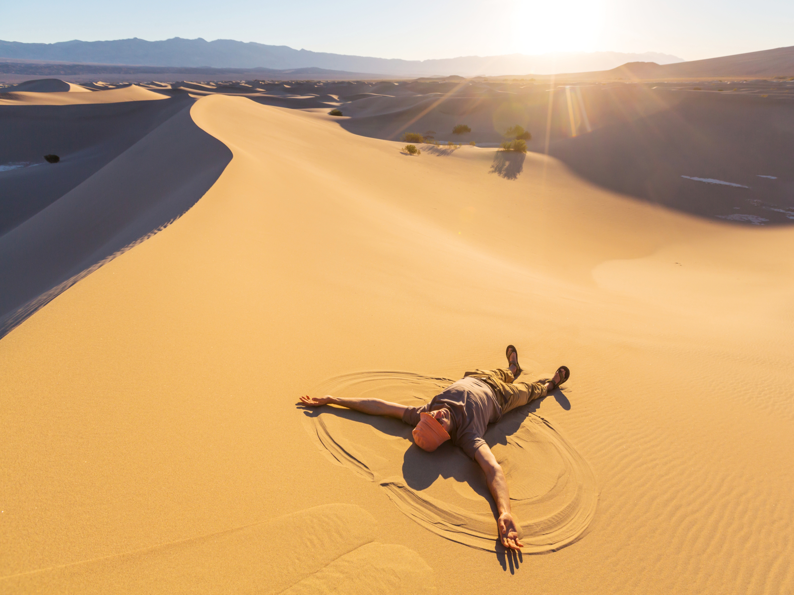 Guy doing sand angels on a dune during the best time to visit Death Valley National Park