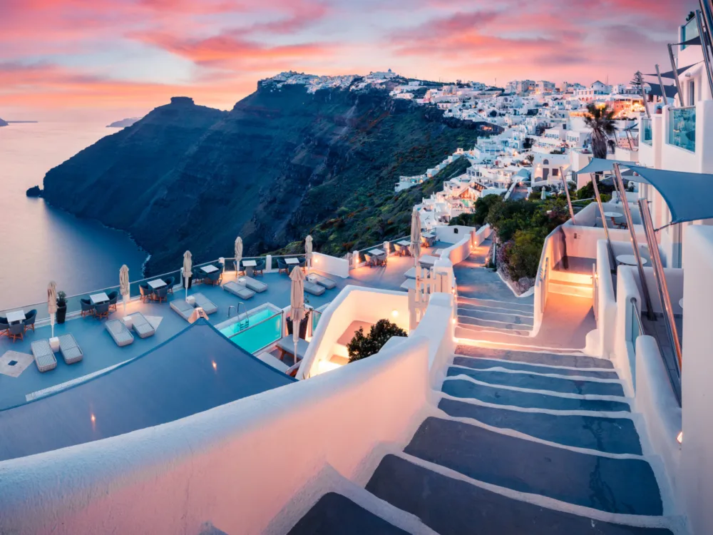 A luxurious dusk at Santorini Island, on a solemn sunset as one of the best places to visit in Greece, with its traditional white structures sitting atop a mountain on a calm sea