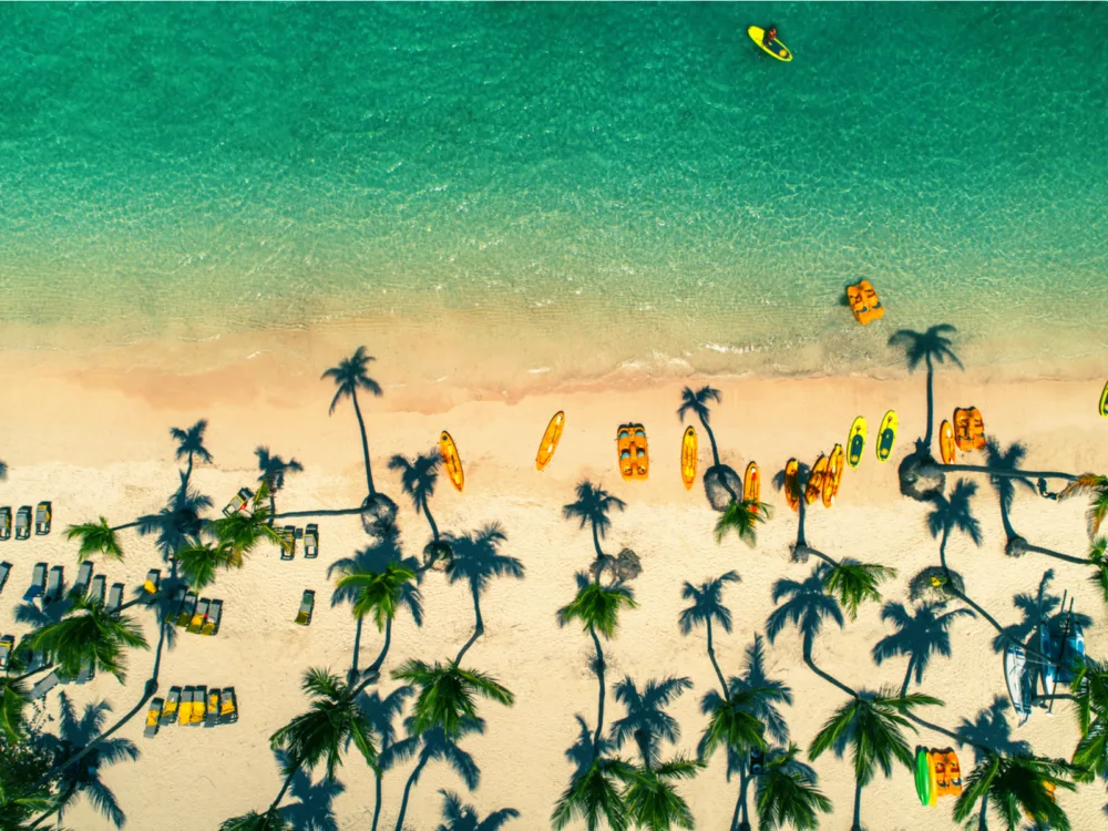 Overhead view on one of the best beaches in the Dominican Republic, Bávaro Beach in Punta Cana where palm trees shadows casted towards the beach and empty sunloungers and paddle boards sit on shore