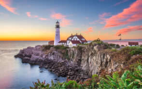 Portland pictured during the best time to visit Maine with a gorgeous sunset in the background and a lighthouse on a rocky cliff