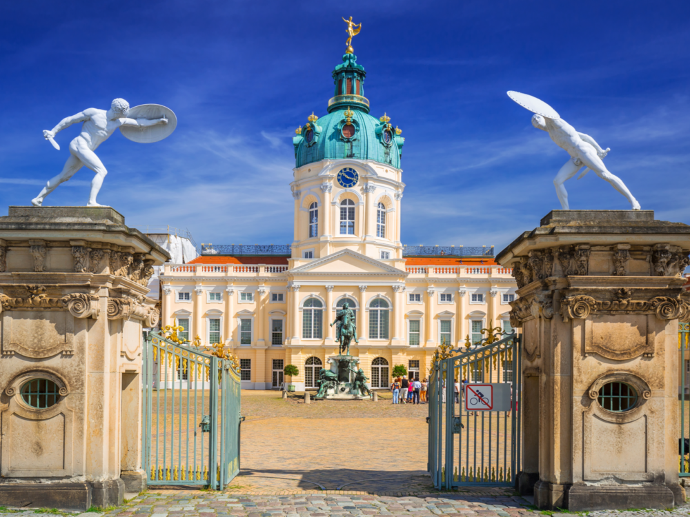Two naked statue of warriors with sword and shield at the gate of Charlottenburg Palace in Berlin, a piece on the best castles in Germany, inside are few tourists gathered beside a statue of a person on a horse