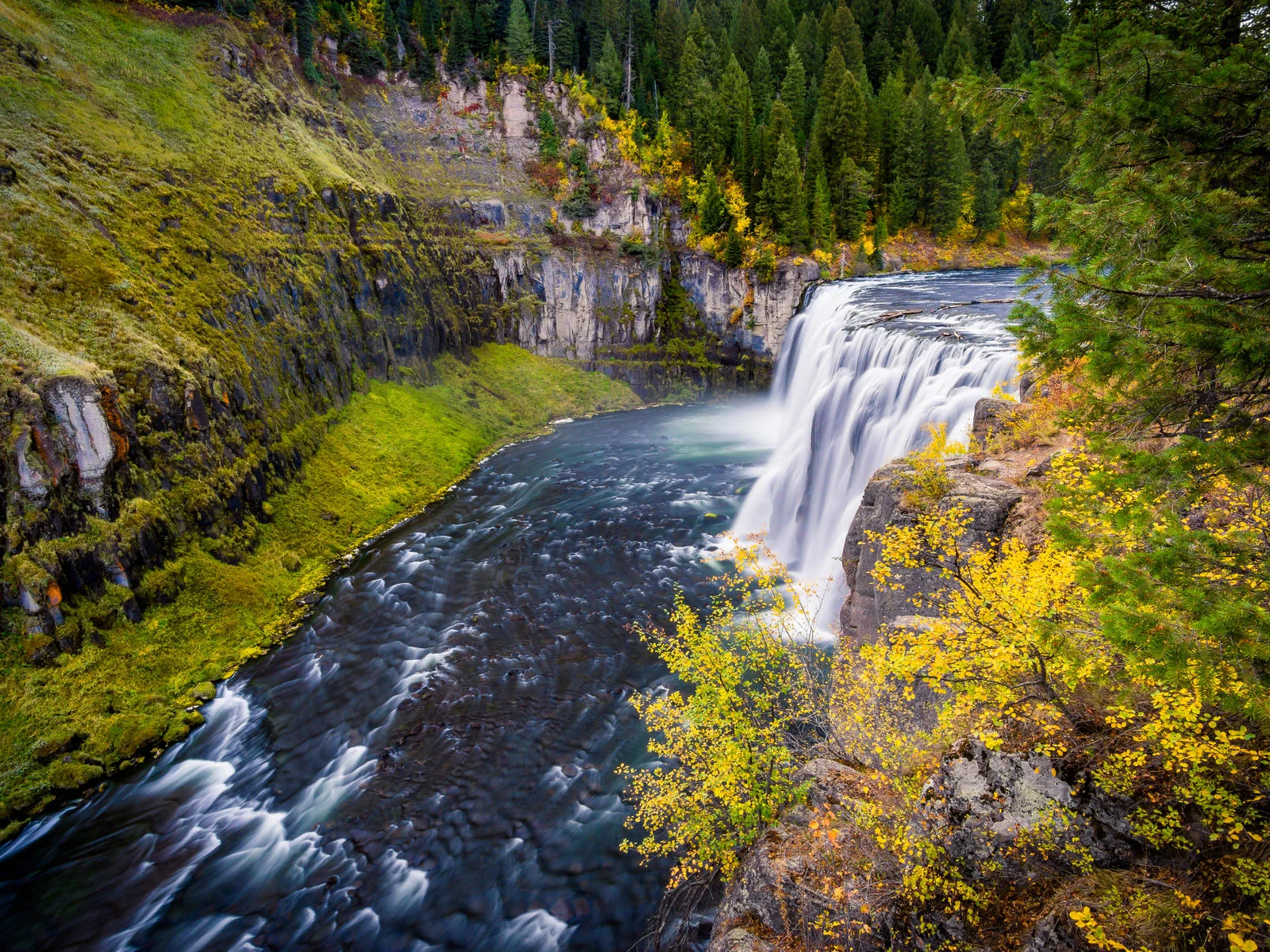 Majestic scene on an Autumn season at Upper Mesa Falls, one of the best things to see in Idaho, where a large stream flows beside moss covered rocks