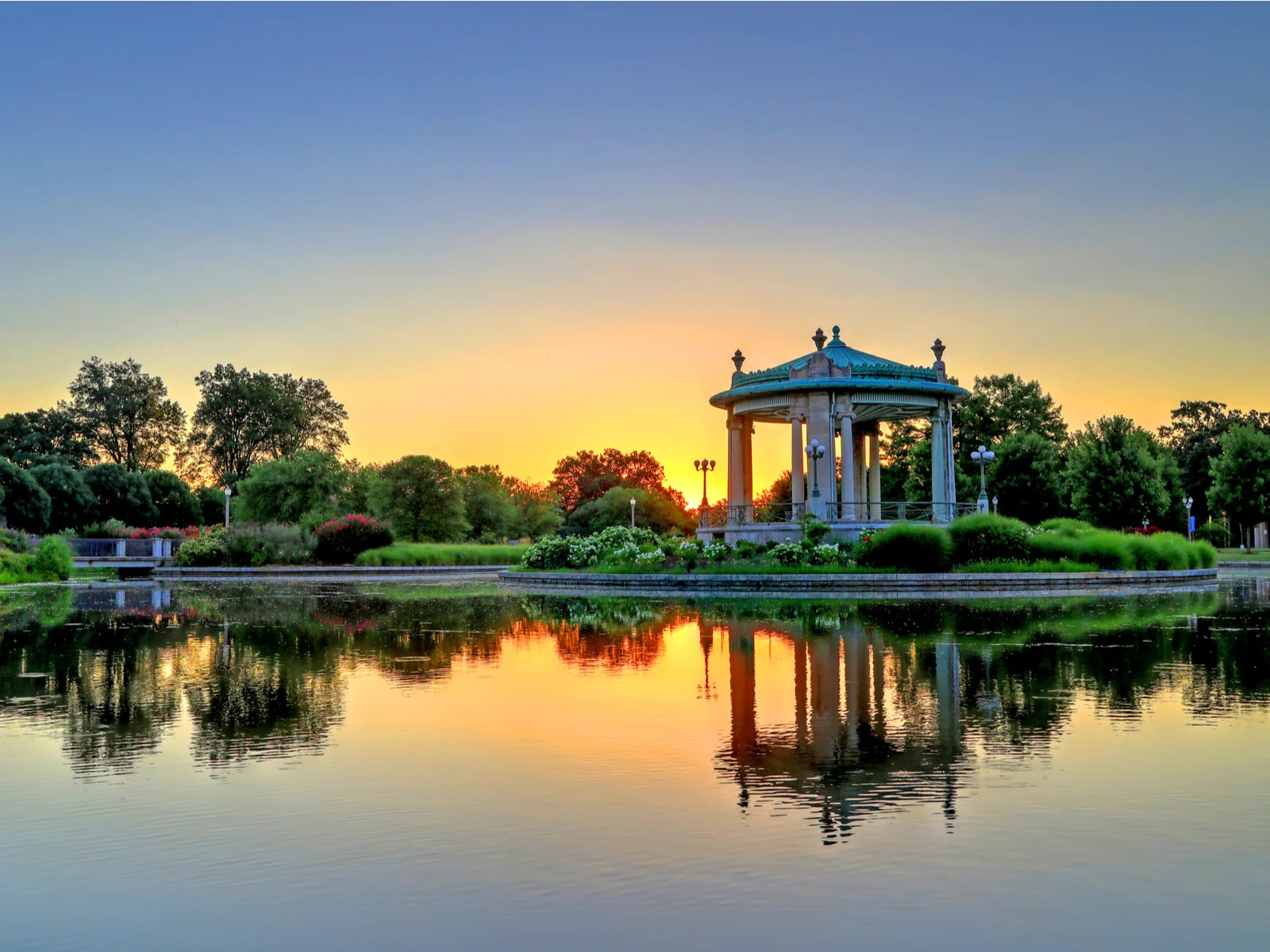 A high contrast picture of the bandstand in Forest Park surrounded by calm waters during sunset, one of the best things to do in St. Louis