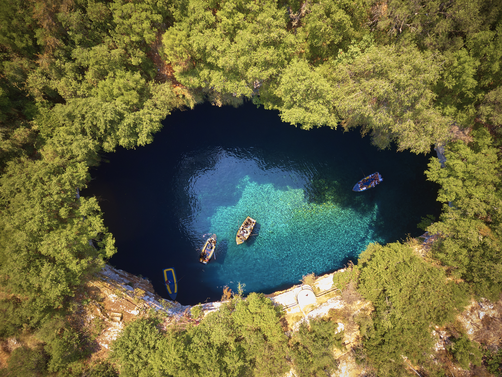 Overhead view on four boats hovering at Melissani Cave ( Melissani Lake) near Sami village in Kefalonia island, a notable place and one of the best places to visit in Greece, with its crater surrounded by lush forest