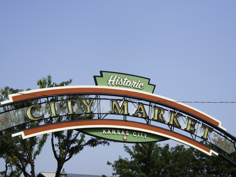 A welcome arch at the Historic City Market in Kansas City with trees and clear blue sky in background, one of the best things to see in Kansas