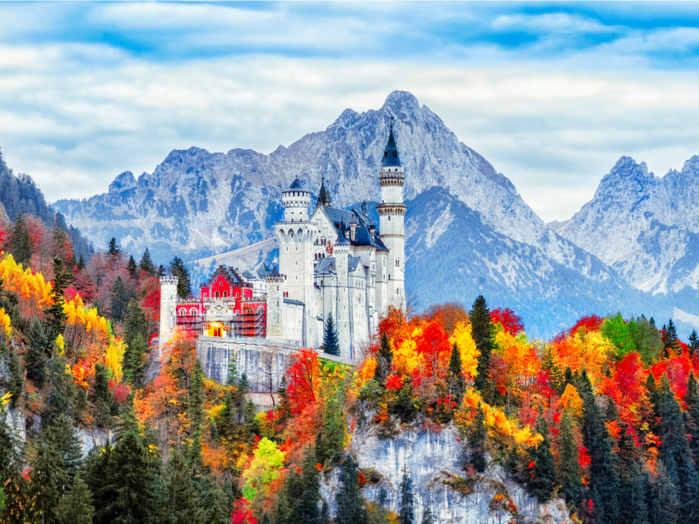 The Neuschwanstein Medieval Castle in Schwangau, one of the best castles in Germany, encircled by vibrant foliage on Autumn and cold tall mountains in background