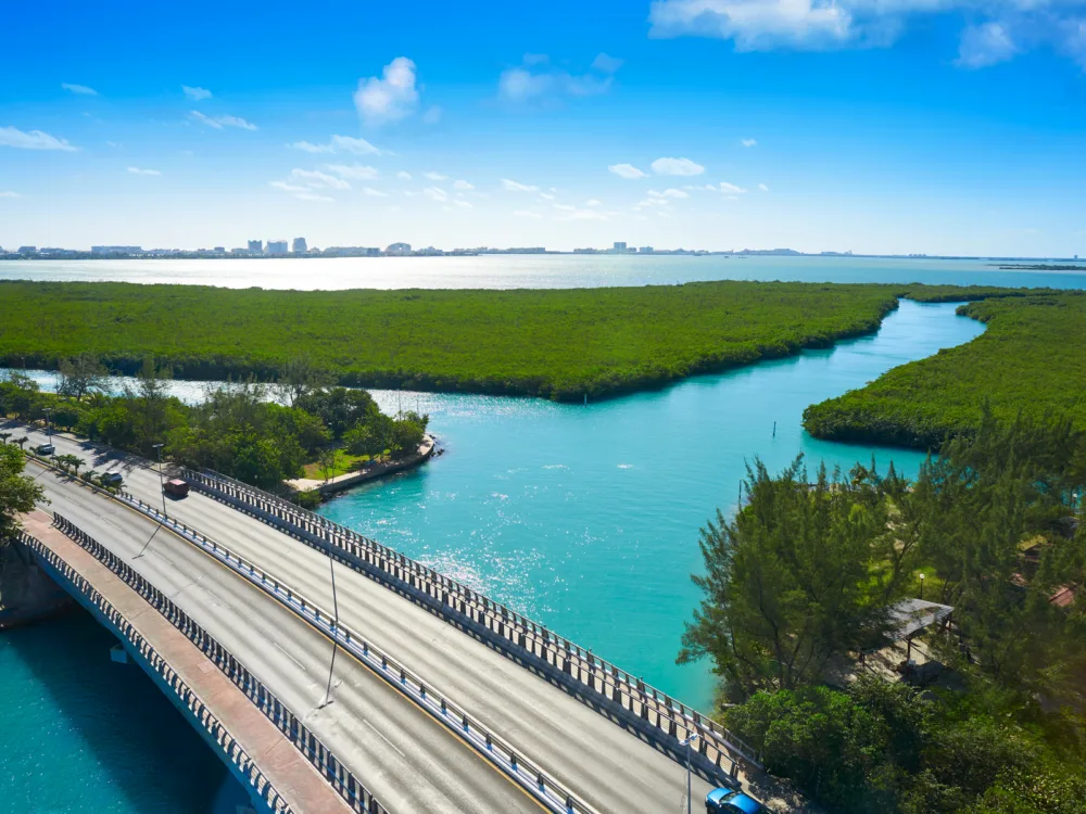 Few cars passing by a bridge traversing the Nichupte Lagoon, one of the best things to do in Cancun, with its thick layers of green Mangroves