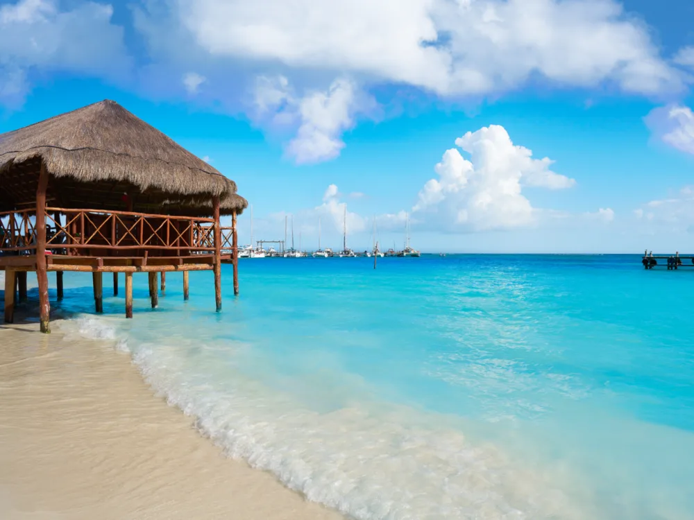 A Tiki Hut on a high tide at Playa Maroma, considered as one of the best beaches in Cancun, with its blue water and docked boats seen in background