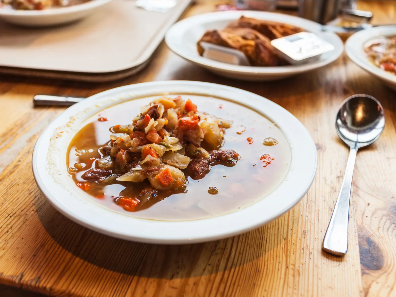 A plate of traditional Kjotsupa Icelandic Lamb Soup with a spoon and other dished blurred in background on a wooden table at Reykjavík Kitchen, known as one of the best restaurants in Iceland