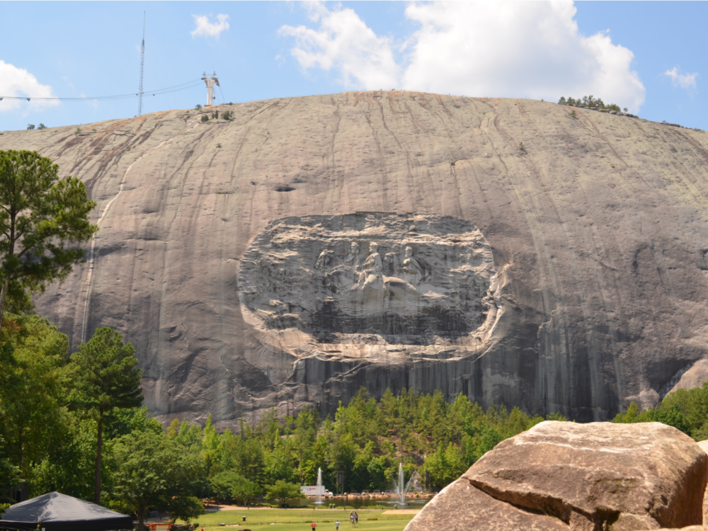 Image of three people mounted on hoses sculpted on the gigantic boulder at Stone Mountain Park, one of the best tourist attractions in Georgia, with a trees and fountains at its foot