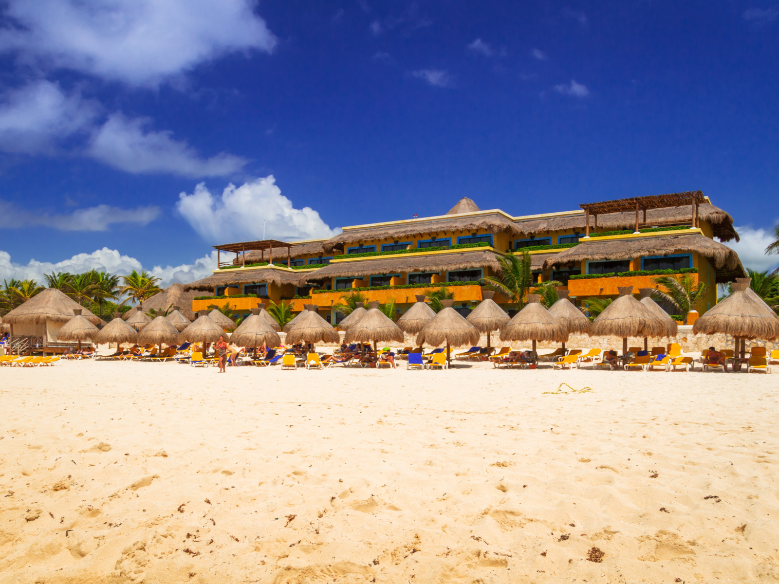 People taking shade under single-pole tiki huts while lying on sun beds during a hot summer day at a resort in Playacar Beach, a pick on the best beaches in Cancun
