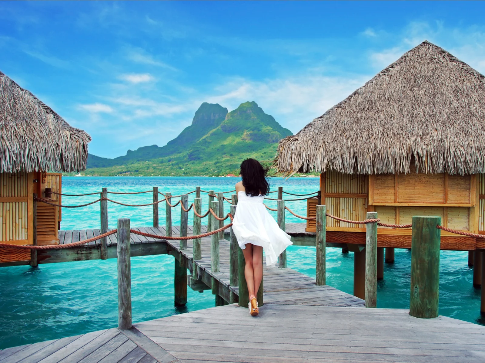 Woman standing on a walkway between huts in one of the best places for an island vacation, Bora Bora