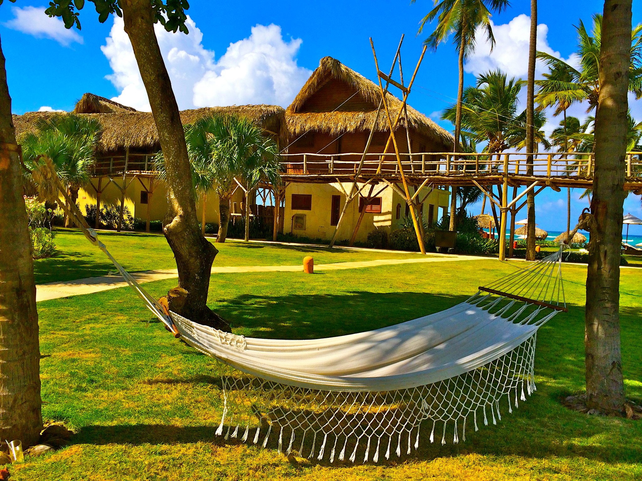 A hammock supported by two trees and native huts with green lawn in Zoetry Agua Punta Cana, one of the best all-inclusive resorts in Punta Cana