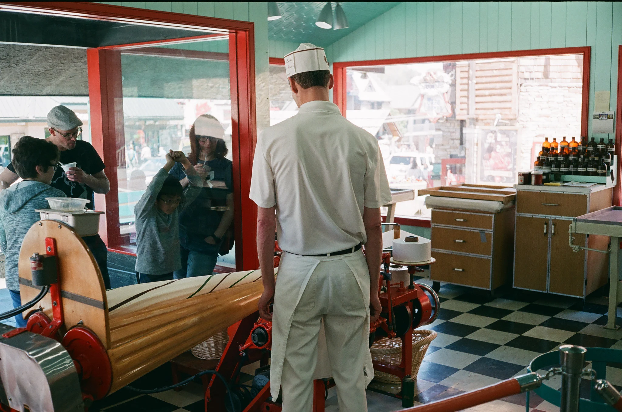 two children and adults waiting for a candy being made using a traditional candy machine operated by a store crew wearing a white uniform in ole smoky candy kitchen, one of the best things to do in gatlinburg, tennessee