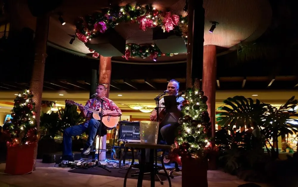 Weldon Kekauoha and Jack Ofoia singing while playing their acoustic guitars on the stage with Christmas lights at Kani Ka Pila Grille during the holiday season, one of the best restaurants in Oahu