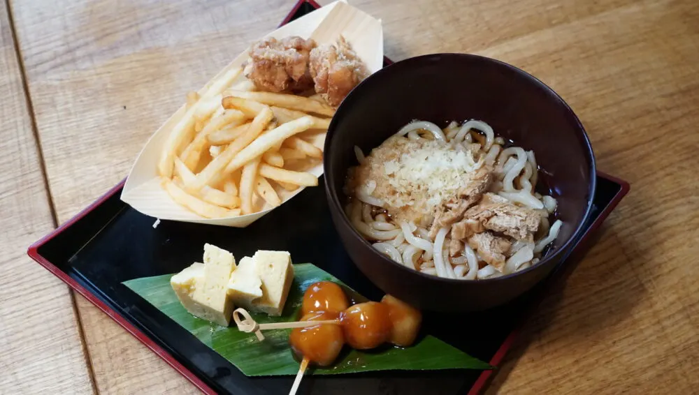 A serving of traditional Japanese noodles, french fries, and other dishes on a wooden table at ZIGU, a famous Japanese restaurant and one of the best restaurants in Oahu, Hawaii