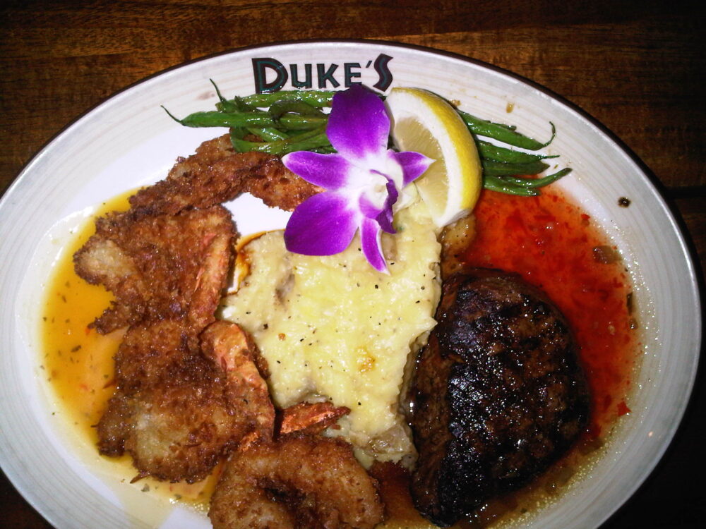 A serving of coffee-crusted steak with coconut shrimp, garlic mashed potatoes, and green beans with lemon and flower at Duke’s Waikiki, a piece on the best restaurants in Oahu
