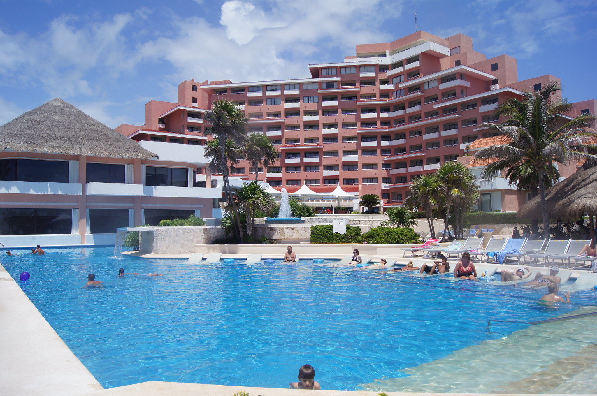 Visitors enjoy swimming and sun bathing on the pool at Omni Cancun Hotel & Villas, titled as one of the best all-inclusive resorts in Mexico, a hot day over its hotel building