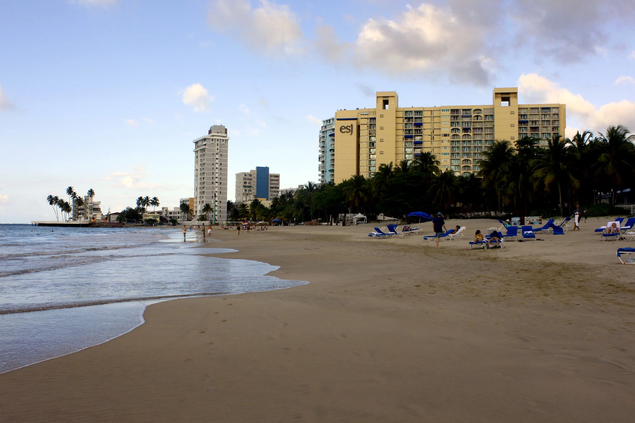 Tourists laying on sun beds at the shore of Playa de Isla Verde, among the best places to visit in Puerto Rico, on a late afternoon, and hotels visible in the background