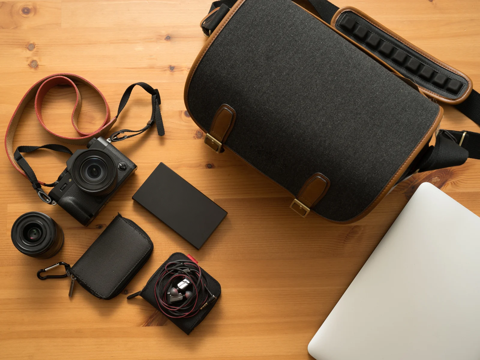 Black digital camera with an orange strap next to one of the best camera bags on a wooden table