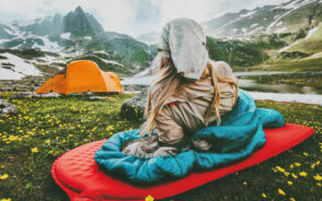 Woman relaxing on a sleeping bag and mat in a field of flowers on one of the best backpack sleeping bags