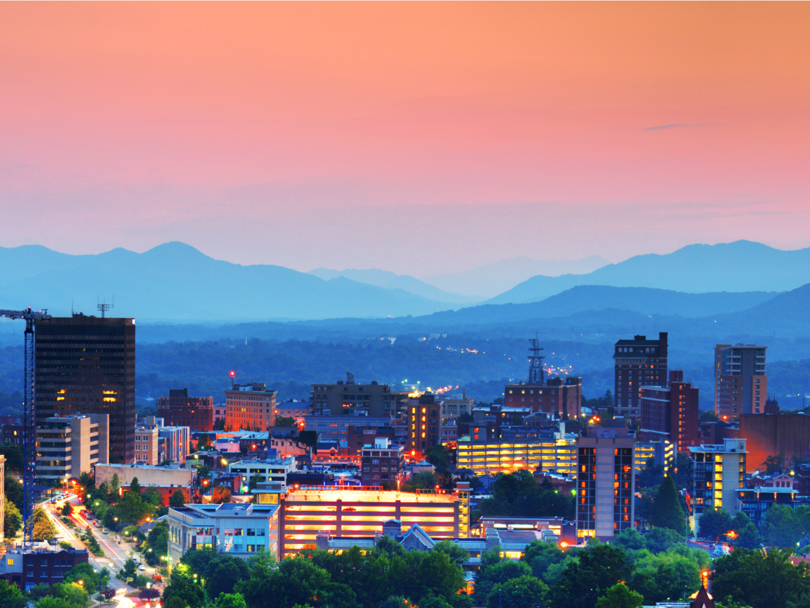 The city of Asheville at dusk and the Blue Ridge Mountains in background displaying the best things to do in Asheville, NC