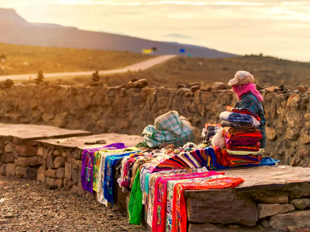 Guy in the the desert with a cloak over his face selling colorful blankets