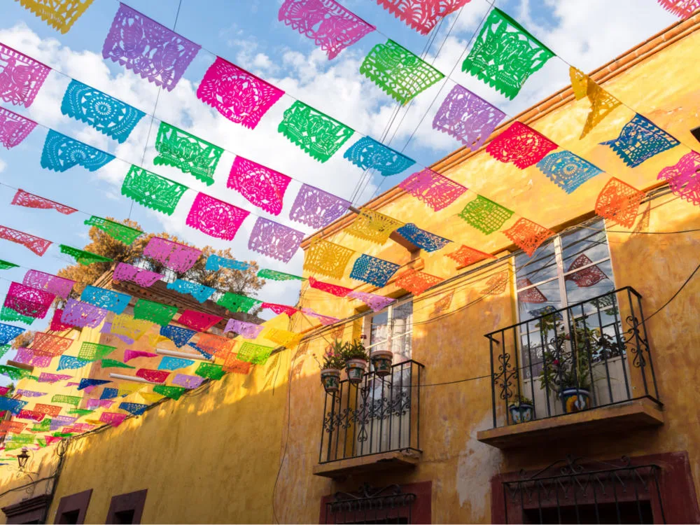 Colorful paper flags hanging above the street between yellow buildings during the best time to visit Mexico City