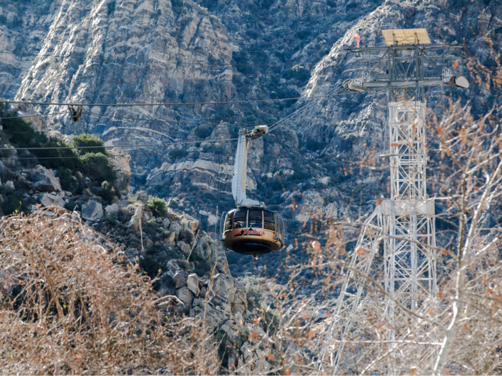 Thrilling sight Palm Springs Aerial Tramway's rotating tram car traversing tight cable ropes and a rocky mountain side in backdrop, one of the best things to do in Palm Springs
