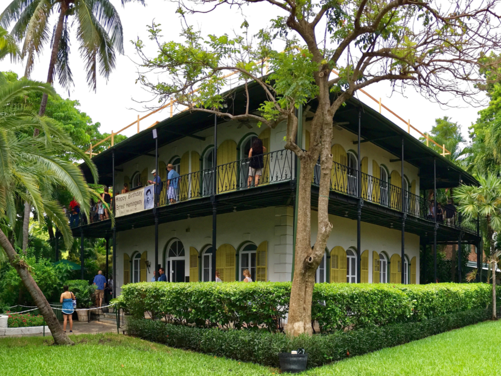 Tourist visiting the historic two storey Ernest Hemingway Home and Museum with trees and neatly landscaped lawn, one of the best things to do in Key West