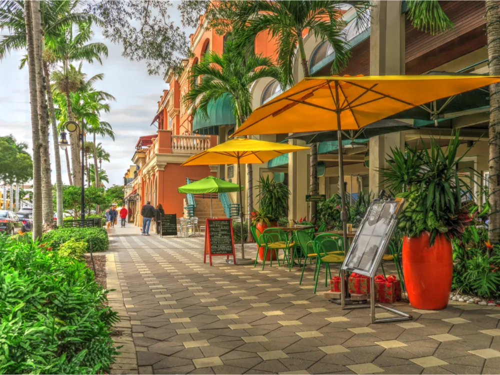 Empty chairs and tables beneath yellow umbrellas of a restaurant on a sidewalk in Naples, Florida, considered one of the most beautiful cities in the US