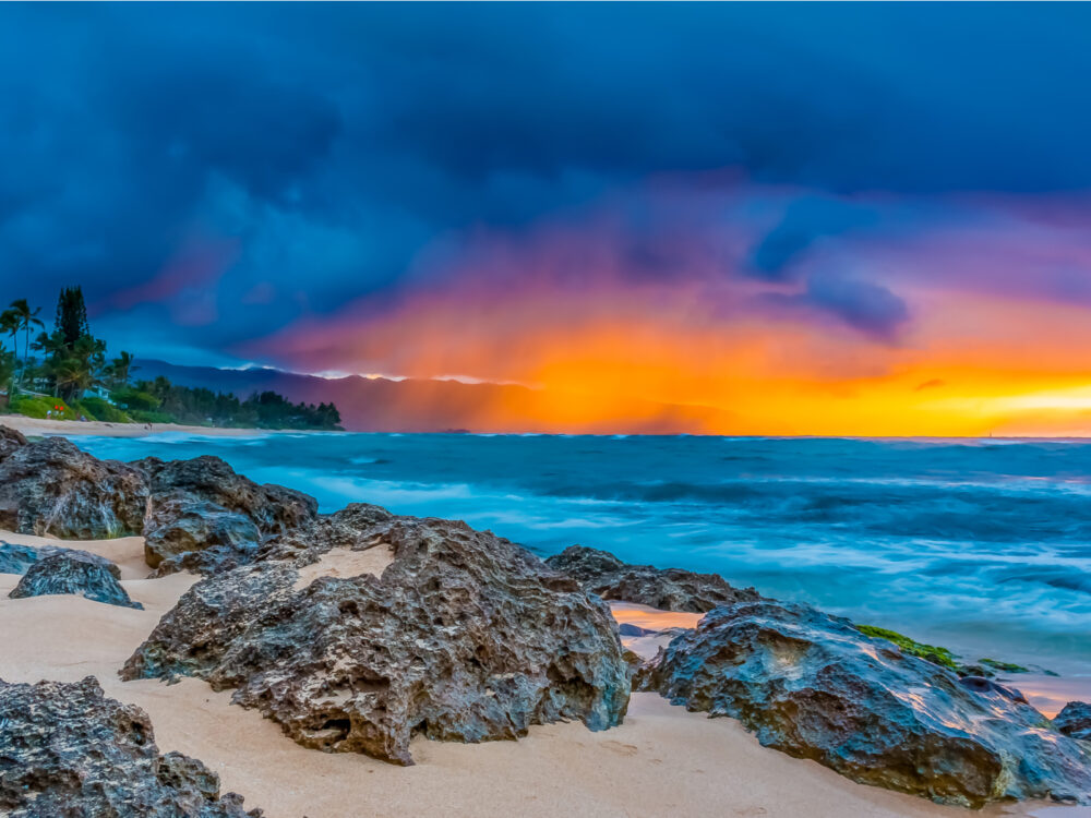 Skies on fire at sunset with rain in the background on the north shore during the best time to visit Oahu