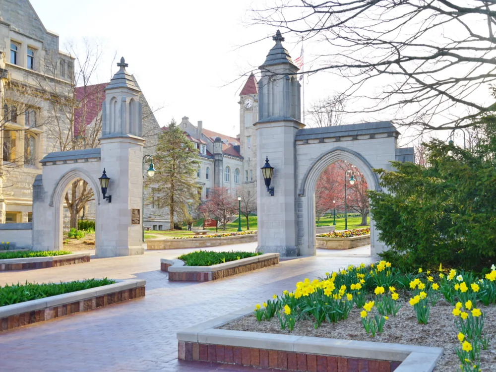 The Sample Gates beside old campus buildings at Indiana University in Indiana, one of the most beautiful college campuses, with vibrant yellow flowers and polish brick pathway