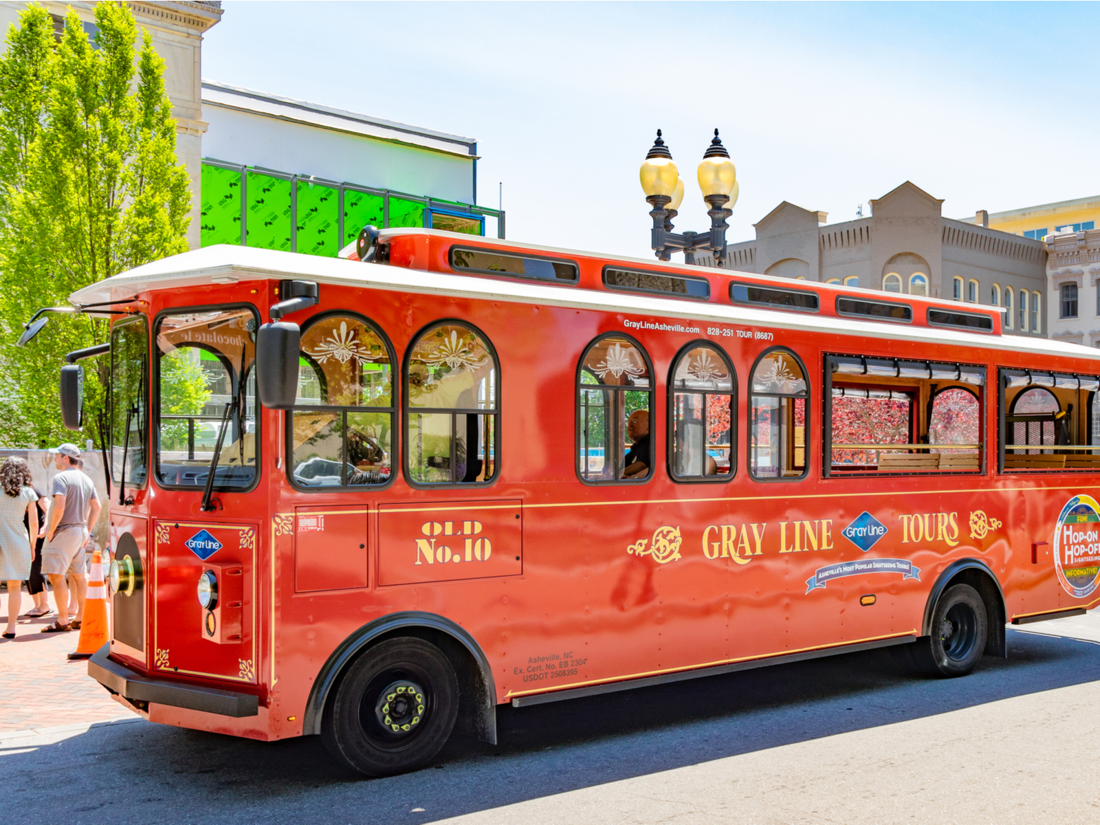 A group of people standing beside a red Gray Line Trolley tour bus, one of the best things to do in Asheville, NC
