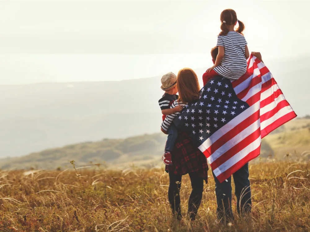A family of four holding an American Flag facing a vast landscape in one of the most iconic places in America