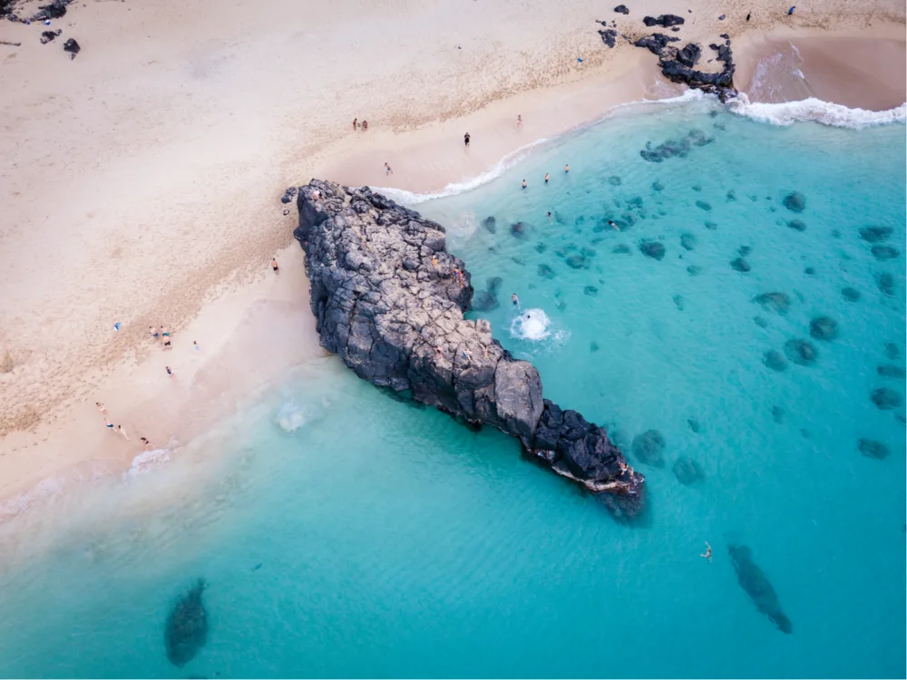 Aerial view on the iconic rock at Waimea Bay Beach Park, a piece on the best beaches in the US, where visitors are seen swimming at the crystal clear turquoise water