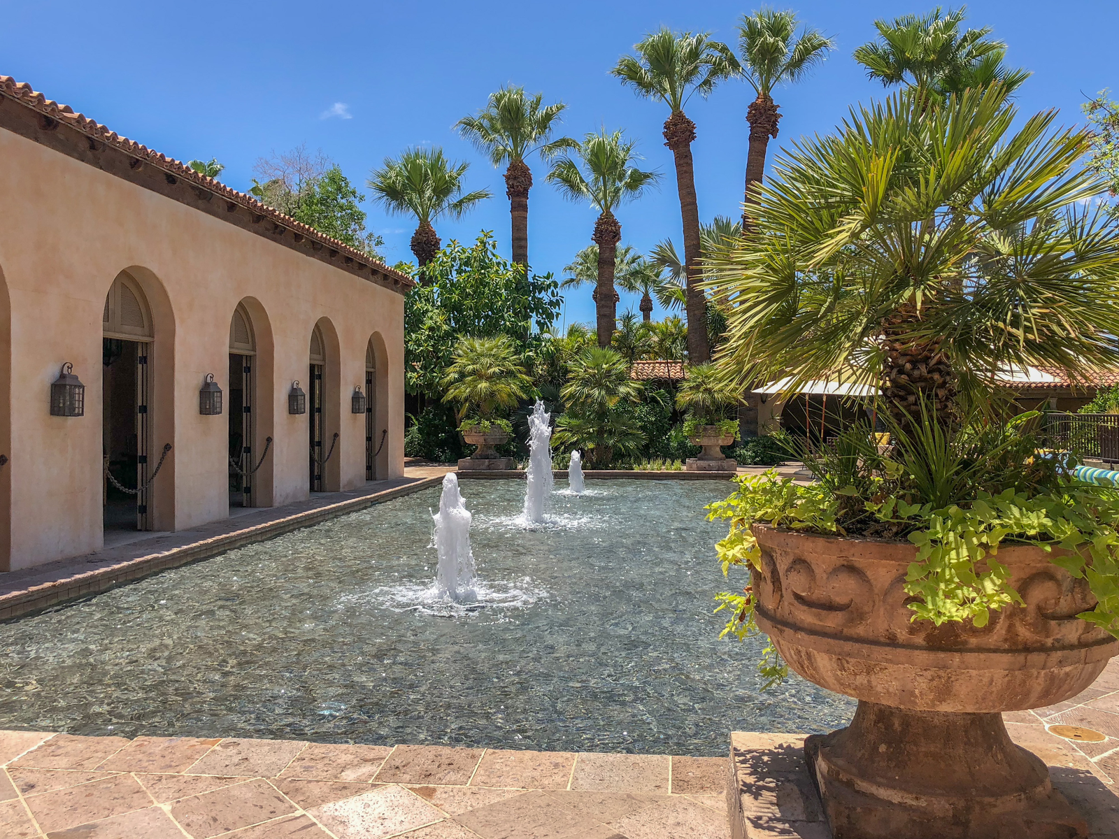 Three fountain heads spouting water by the pool and small palm trees planted in an antique pot at Royal Palms Resort & Spa, one of the best all-inclusive resorts in the U.S.