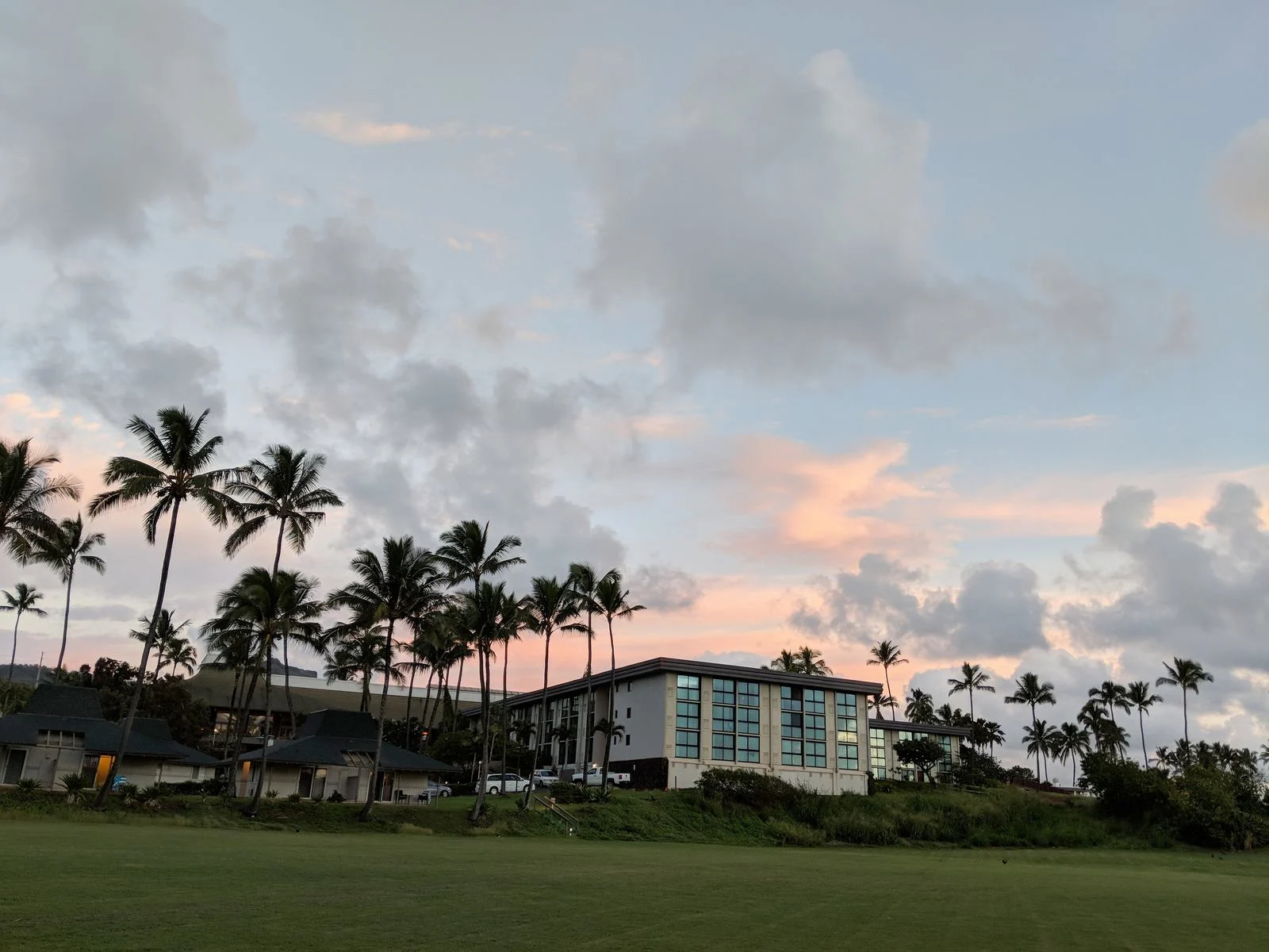 Early morning sky over Hilton Garden Inn Kauai Wailua Bay, photographed from the shore as a piece on the best hotels in Kauai, where cars are parked beside its structure