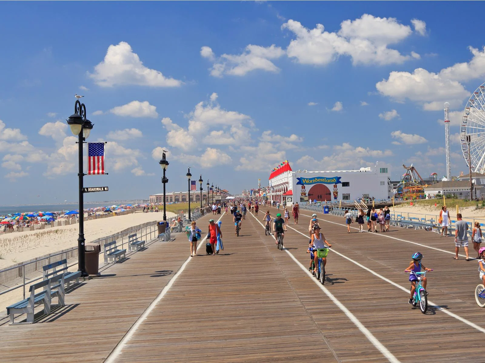 Children and adults biking along the famous wide board at Ocean City in New Jersey, a piece on the best beaches on the East Coast, with fun amusement park on one side and busy beach on the other